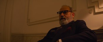 Movie still from “Magic Mike's Last Dance” (2023), directed by Steven Soderbergh – An older man with a beard wearing glasses and a tie; Close Up shot, Low angle