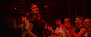 Movie still from “Magic Mike's Last Dance” (2023), directed by Steven Soderbergh – A group of people are gathered around a woman singing; Medium shot, Low angle