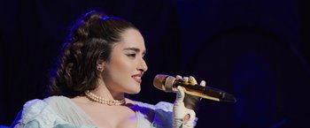 Movie still from “Magic Mike's Last Dance” (2023), directed by Steven Soderbergh – A woman in a white dress holding a microphone; Close Up shot, Over the shoulder angle