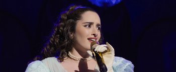 Movie still from “Magic Mike's Last Dance” (2023), directed by Steven Soderbergh – A woman in a white dress is singing into a microphone; Close Up shot, High angle