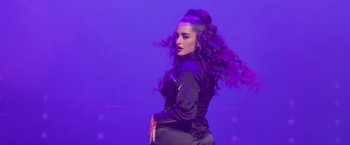 Movie still from “Magic Mike's Last Dance” (2023), directed by Steven Soderbergh – A woman in a black jacket is on a purple stage; Medium shot, Low angle