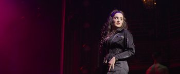 Movie still from “Magic Mike's Last Dance” (2023), directed by Steven Soderbergh – A woman in a black dress standing on a stage; Medium shot, Over the shoulder angle