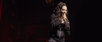 Movie still from “Magic Mike's Last Dance” (2023), directed by Steven Soderbergh – A woman with long curly hair singing into a microphone; Medium shot, High angle