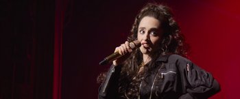 Movie still from “Magic Mike's Last Dance” (2023), directed by Steven Soderbergh – A woman holding a microphone in her hand; Close Up shot, High angle