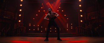 Movie still from “Magic Mike's Last Dance” (2023), directed by Steven Soderbergh – A man in black pants and a black shirt on a stage with red lights; Wide shot, Low angle