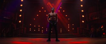 Movie still from “Magic Mike's Last Dance” (2023), directed by Steven Soderbergh – A man standing in front of a stage lit by lights; Wide shot, Low angle