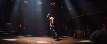 Movie still from “Magic Mike's Last Dance” (2023), directed by Steven Soderbergh – A man wearing a helmet is standing on a stage; Wide shot, Over the shoulder angle