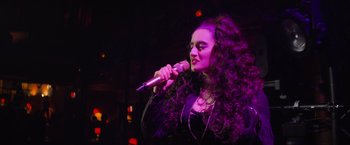 Movie still from “Magic Mike's Last Dance” (2023), directed by Steven Soderbergh – A woman with long curly hair is holding a microphone; Close Up shot, Low angle