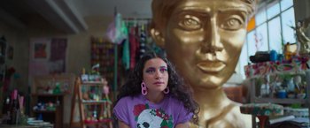 Movie still from “Making It Up” (2023), directed by Guillermo Calderón – A woman in a purple shirt is in front of a gold statue; Close Up shot, Low angle