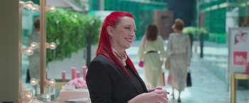 Movie still from “Making It Up” (2023), directed by Guillermo Calderón – A woman with long red hair is smiling for the camera; Medium shot, Over the shoulder angle
