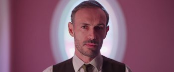 Movie still from “Making It Up” (2023), directed by Guillermo Calderón – A person wearing a suit and tie; Close Up shot, Low angle