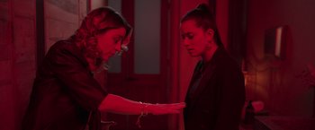 Movie still from “Making It Up” (2023), directed by Guillermo Calderón – Two women in a dark room one is holding a hand out to the other; Medium shot, Over the shoulder angle