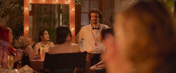 Movie still from “Making It Up” (2023), directed by Guillermo Calderón – A man standing in front of a mirror in front of other people; Medium shot, Over the shoulder angle