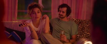 Movie still from “Making It Up” (2023), directed by Guillermo Calderón – A man and a woman sitting on a couch with a glass of beer; Medium shot, Over the shoulder angle