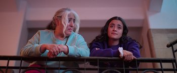 Movie still from “Making It Up” (2023), directed by Guillermo Calderón – Two women sitting next to a railing looking at each other; Medium shot, Low angle