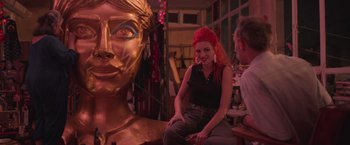 Movie still from “Making It Up” (2023), directed by Guillermo Calderón – A woman sitting next to a statue of a woman's face; Medium shot, Low angle