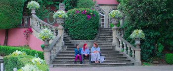 Movie still from “Making It Up” (2023), directed by Guillermo Calderón – Three people sitting on the steps in front of a building; Wide shot, High angle