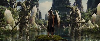 Movie still from “Maleficent” (2014), directed by Robert Stromberg – A woman with a large angel wings standing on a rock in the middle of a river; Wide shot, High angle