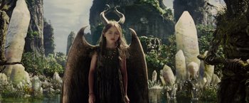 Movie still from “Maleficent” (2014), directed by Robert Stromberg – A young girl dressed as maleficent in front of a mountain; Medium shot, High angle