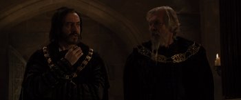 Movie still from “Maleficent” (2014), directed by Robert Stromberg – Two men dressed in medieval garb in a dark room; Medium shot, Over the shoulder angle