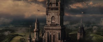 Movie still from “Maleficent” (2014), directed by Robert Stromberg – An old castle with a clock tower and a tower with a flag on it; Extreme Wide shot, Low angle
