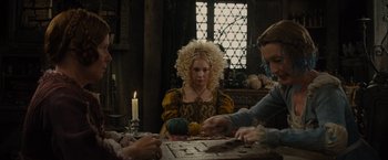 Movie still from “Maleficent” (2014), directed by Robert Stromberg – A woman with blonde curly hair sitting at a table; Medium shot, Over the shoulder angle
