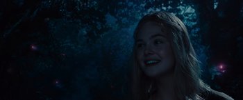 Movie still from “Maleficent” (2014), directed by Robert Stromberg – A girl is smiling in the dark with trees in the background; Close Up shot, Over the shoulder angle