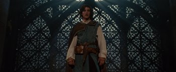 Movie still from “Maleficent” (2014), directed by Robert Stromberg – A young man in medieval garb standing in front of a wooden structure; Medium shot, Low angle