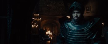 Movie still from “Maleficent” (2014), directed by Robert Stromberg – A man in a suit of armor stands in front of a fireplace; Medium shot, Over the shoulder angle