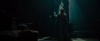 Movie still from “Maleficent” (2014), directed by Robert Stromberg – A woman standing in front of a window in a dark room; Wide shot, Over the shoulder angle