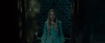 Movie still from “Maleficent” (2014), directed by Robert Stromberg – A woman in a blue dress standing in front of a wall; Medium shot, Low angle