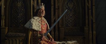 Movie still from “Maleficent: Mistress of Evil” (2019), directed by Joachim Rønning – A man sitting on top of a chair holding a sword; Medium shot, Low angle