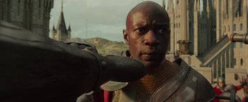 Movie still from “Maleficent: Mistress of Evil” (2019), directed by Joachim Rønning – A black man in a red and gold outfit holding a black object; Close Up shot, Over the shoulder angle