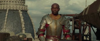 A man wearing a suit of armor standing next to a building