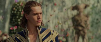 Movie still from “Maleficent: Mistress of Evil” (2019), directed by Joachim Rønning – A man with long brown hair wearing a blue and gold jacket; Close Up shot, Over the shoulder angle