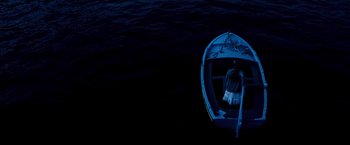 Movie still from “Mamma Mia!” (2008), directed by Phyllida Lloyd – A person sitting on a boat in the middle of the night; Extreme Wide shot, Overhead angle