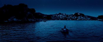 Movie still from “Mamma Mia!” (2008), directed by Phyllida Lloyd – A person in a boat in a body of water at night; Extreme Wide shot, High angle