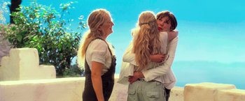 Movie still from “Mamma Mia!” (2008), directed by Phyllida Lloyd – A group of people hugging each other in front of a blue sky; Medium shot, Over the shoulder angle