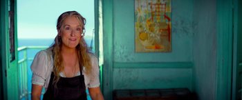 Movie still from “Mamma Mia!” (2008), directed by Phyllida Lloyd – A woman in a black apron is smiling; Close Up shot, Low angle