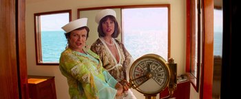 Movie still from “Mamma Mia!” (2008), directed by Phyllida Lloyd – Two women dressed in traditional clothing are standing next to a clock; Medium shot, Low angle