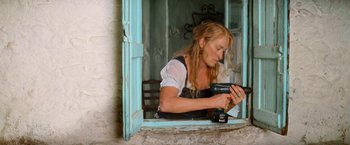 Movie still from “Mamma Mia!” (2008), directed by Phyllida Lloyd – A woman holding a drill in front of an open window; Medium shot, Low angle