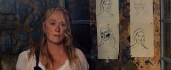Movie still from “Mamma Mia!” (2008), directed by Phyllida Lloyd – A woman standing in front of a drawing of a woman's face; Close Up shot, Over the shoulder angle