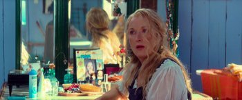 Movie still from “Mamma Mia!” (2008), directed by Phyllida Lloyd – A woman sitting in front of a table with food on top of it; Close Up shot, Over the shoulder angle