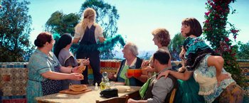 Movie still from “Mamma Mia!” (2008), directed by Phyllida Lloyd – A group of people sitting around a table; Wide shot, Over the shoulder angle