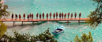 Movie still from “Mamma Mia!” (2008), directed by Phyllida Lloyd – A group of people standing on a bridge over a body of water; Extreme Wide shot, High angle