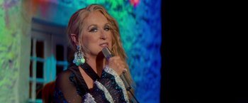Movie still from “Mamma Mia!” (2008), directed by Phyllida Lloyd – A person holding a microphone on a stage; Close Up shot, Over the shoulder angle