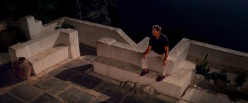 Movie still from “Mamma Mia!” (2008), directed by Phyllida Lloyd – A man sitting on a stone wall at night; Wide shot, High angle