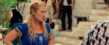 Movie still from “Mamma Mia!” (2008), directed by Phyllida Lloyd – A woman in a blue dress is standing on some steps; Close Up shot, Over the shoulder angle