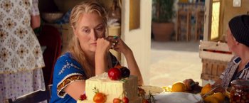 Movie still from “Mamma Mia!” (2008), directed by Phyllida Lloyd – A woman sitting in front of a cake on top of a table; Close Up shot, Over the shoulder angle