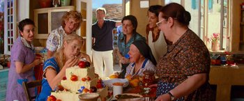Movie still from “Mamma Mia!” (2008), directed by Phyllida Lloyd – A group of people standing around a table with a cake on it; Medium shot, Over the shoulder angle